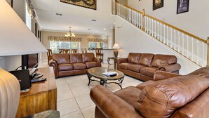 A spacious living room with leather sofas, a coffee table, and a staircase with a railing. - 5 STAR REVIEWED SOUTH FACING LUXURY GOLF AND DISNEY VILLA ON GATED COMMUNITY (Davenport)
