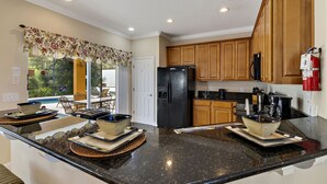 A kitchen with granite countertops, wooden cabinets, and a black refrigerator. - 5 STAR REVIEWED SOUTH FACING LUXURY GOLF AND DISNEY VILLA ON GATED COMMUNITY (Davenport)