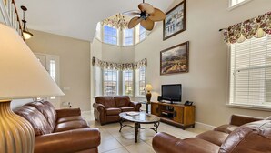 A spacious living room with leather sofas, a coffee table, a television, and a chandelier. - 5 STAR REVIEWED SOUTH FACING LUXURY GOLF AND DISNEY VILLA ON GATED COMMUNITY (Davenport)
