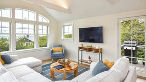 Uma sala de estar moderna com uma televisão grande, assentos confortáveis e vista para o exterior.