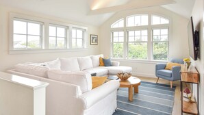 Uma sala de estar espaçosa com um sofá branco modular, uma poltrona azul e uma mesa de centro de madeira.