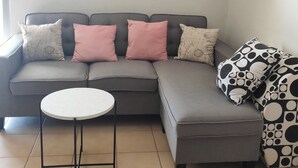 A living room with a grey sofa, a small round table, and a patterned pillow. - Sanctuary for family and friends (Balcatta)