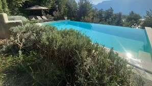 En klarblå pool med solstolar och en liten paviljong, omgiven av frodig grönska och berg i bakgrunden.
