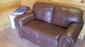 Ein braunes Ledersofa mit Kissen, ein kleiner weißer Tisch mit einer Zeitschrift und eine Holzwand.