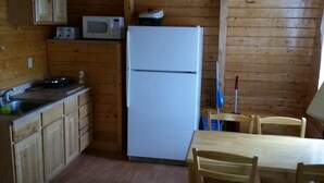 Eine kleine Küche mit Holzwänden, einem weißen Kühlschrank, einer Mikrowelle, einem Spülbecken und einem Essbereich mit Holztischen und einer Tischplatte.