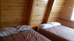 Eine Hütte mit zwei Holzbettgestellen mit jeweils einem Kissen und einer gesteppten Decke.