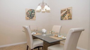 A dining area with a glass table, four chairs, a chandelier, and two wall-mounted artworks. - Indulge in Endless Activities: Tennis, Golf, Pools, and More at Treviso Bay (Naples)