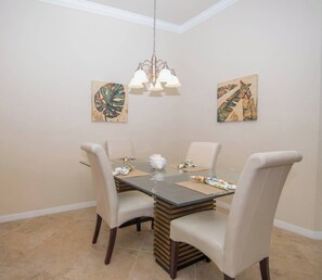 A dining area with a glass table, four chairs, a chandelier, and two wall-mounted artworks. - Indulge in Endless Activities: Tennis, Golf, Pools, and More at Treviso Bay (Naples)