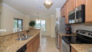 A kitchen with granite countertops, stainless steel appliances, wooden cabinets, and a dining area with a table and chairs. - Indulge in Endless Activities: Tennis, Golf, Pools, and More at Treviso Bay (Naples)