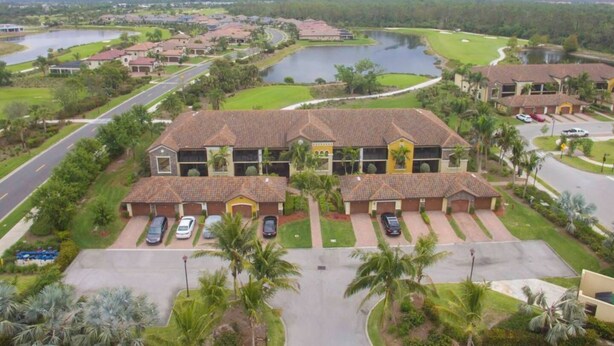 A residential area with a large building featuring multiple parking spaces and a golf course in the background. - Indulge in Endless Activities: Tennis, Golf, Pools, and More at Treviso Bay (Naples)