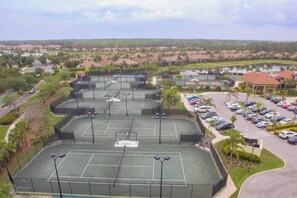 A multi-level parking structure with multiple lanes and a tennis court in the foreground. - Indulge in Endless Activities: Tennis, Golf, Pools, and More at Treviso Bay (Naples)