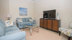 A living room with a sofa, a glass coffee table, a television on a cabinet, and a ceiling fan. - Indulge in Endless Activities: Tennis, Golf, Pools, and More at Treviso Bay (Naples)