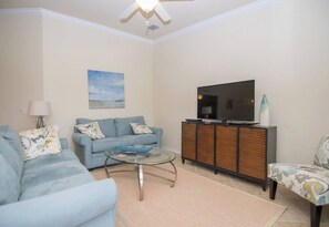 A living room with a sofa, a glass coffee table, a television on a cabinet, and a ceiling fan. - Indulge in Endless Activities: Tennis, Golf, Pools, and More at Treviso Bay (Naples)