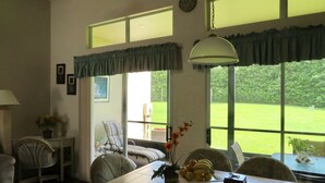 A dining area with a table, chairs, a hanging light fixture, and a view of a green landscape through large windows. - Unique style 2 BR/2 BA townhouse in Disney Area (Kissimmee)