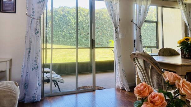 A room with a large sliding glass door leading to a garden. There is a chair and a table with a vase of flowers. - Unique style 2 BR/2 BA townhouse in Disney Area (Kissimmee)