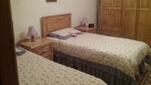 A bedroom with two single beds, wooden headboards, a nightstand with a lamp, a wardrobe, and a framed picture on the wall.