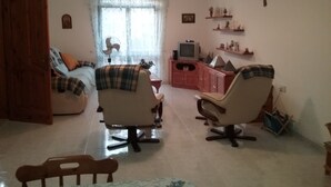 A living room with a sofa, two armchairs, a TV, and a fan.