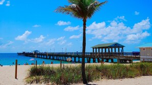 A beach with a palm tree, a pier, and a lifeguard station. - BY THE SEA VACATION VILLAS 3 BED POOL/ BEACH AT END OF STREET (Lauderdale-by-the-Sea)
