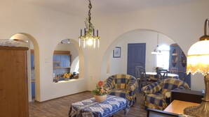 Una sala de estar con un sofá, una mesa de centro con un centro de flores y una araña. Hay puertas arqueadas que dan a otras habitaciones.