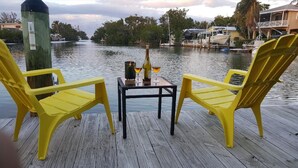 En træbrygge med to gule stole og et bord med en flaske og glas.