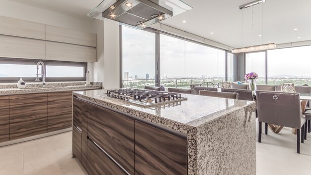 Una cocina moderna con una isla grande, armarios de madera oscura y vistas a la ciudad.