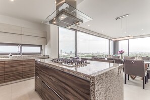 Cocina moderna con una isla grande, armarios de madera oscura y vistas de la ciudad a través de amplios ventanales.