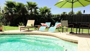 A swimming pool with lounge chairs and an umbrella.