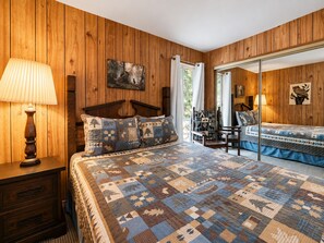 Ein Schlafzimmer mit einer holzverkleideten Wand, einem Bett mit Quiltdecke, einem Nachttisch mit Lampe und einem Sessel mit gepolstertem Rücken.