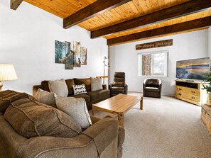 A living room with a brown sofa, a wooden coffee table, a TV, and artwork on the wall.