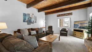Ein Wohnzimmer mit Holzboden, einer Sofagarnitur, einem Couchtisch, einem Fernseher und einer Wand mit Kunstwerken.