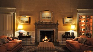 A cozy living room with a fireplace, two armchairs, a sofa, and a coffee table. There are two lamps on side tables and a bookshelf with decorative items. - Historic 2000 Acre Country Estate in Rural Ayrshire, near Troon and Prestwick. (Hurlford)