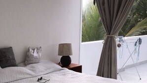 Un dormitorio moderno con una cama grande, una mesita de noche, una lámpara y vistas al exterior a través de una ventana con cortinas.