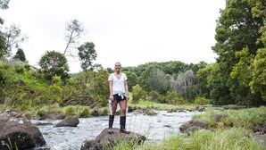 A person standing by a river with rocks and greenery in the background. - Byron Hinterland Retreat - Honeymoon (Repentance Creek)