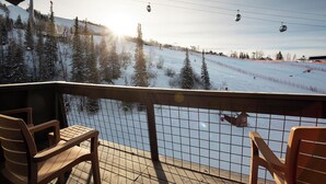A ski resort view from a covered area with wooden chairs, a snow-covered slope, and a ski lift in the background. - SE068 | Amazing views | Hot Tub | Winter Shuttle | Ski In/Out (Steamboat Springs)