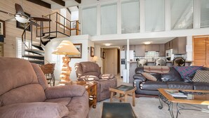 A spacious living area with a sofa, armchairs, and a coffee table. A staircase leads to an upper level, and a kitchen is visible in the background. - SE068 | Amazing views | Hot Tub | Winter Shuttle | Ski In/Out (Steamboat Springs)