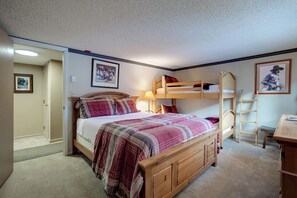 A bedroom with a bunk bed, a wooden dresser, a desk, and a ladder.