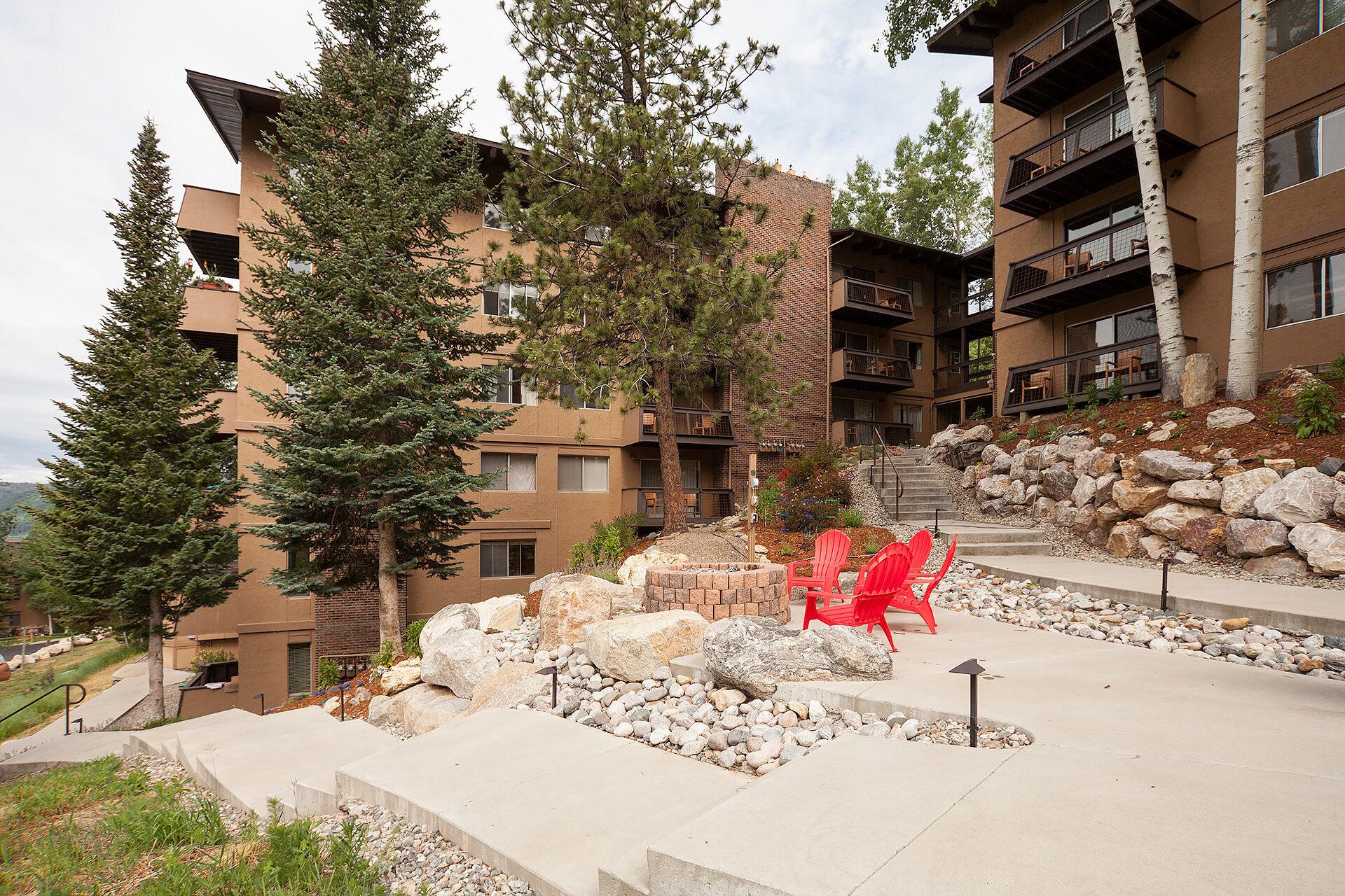 A modern building with multiple balconies and a landscaped outdoor area with red chairs and a fire pit.