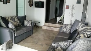 A living room with a grey sofa set, a small table, and a TV mounted on the wall.
