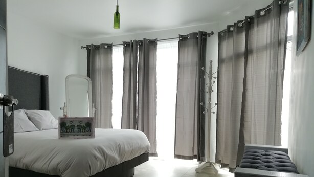 A bedroom with a bed, a bedside table with a mirror, a dresser, a bench, and a window with curtains.