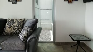 A living room with a grey sofa, patterned cushions, a glass door leading to a balcony, and a small table.