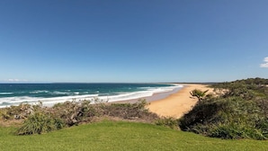 A beach with a clear view of the ocean and a grassy area in the foreground.
