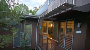 Un edificio moderno con terraza de madera, ventanas amplias y un pequeño espacio exterior con plantas.