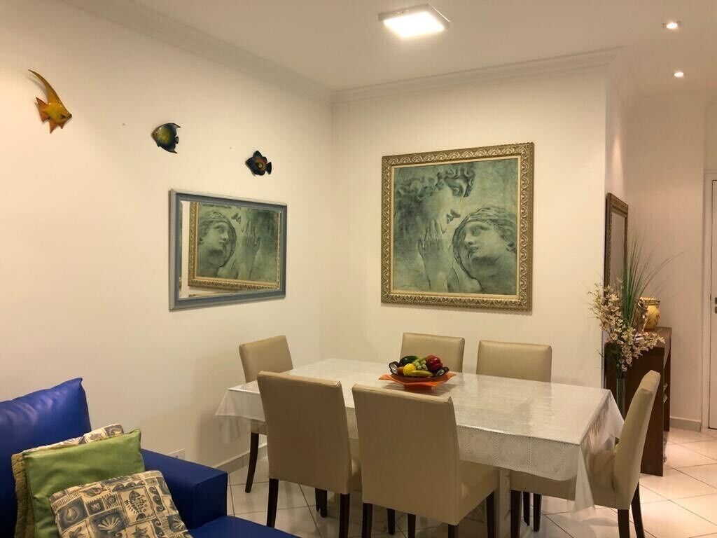 A dining area with a table set for six, surrounded by chairs, and two framed artworks on the wall.