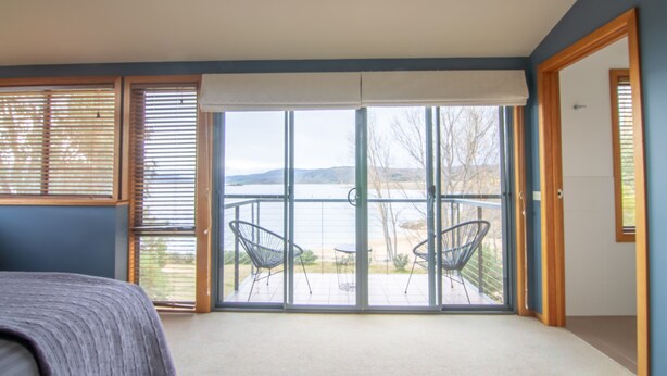 A bedroom with a large sliding glass door leading to a balcony with two chairs and a table.