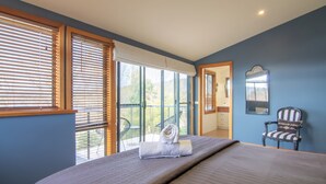 A bedroom with a bed, a chair, a window with blinds, and a door leading to a balcony.