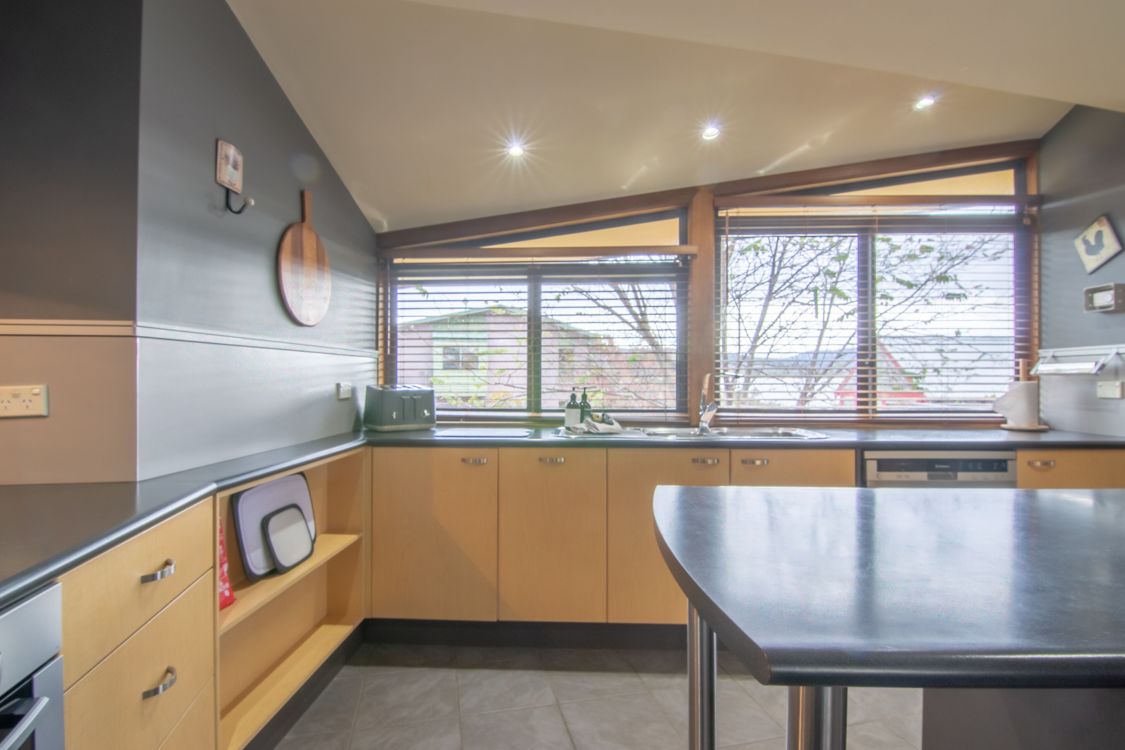 A modern kitchen with wooden cabinets, a black countertop, and a window with blinds.
