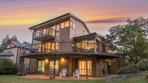 A modern two-story house with a covered patio area, outdoor seating, and a large glass window.