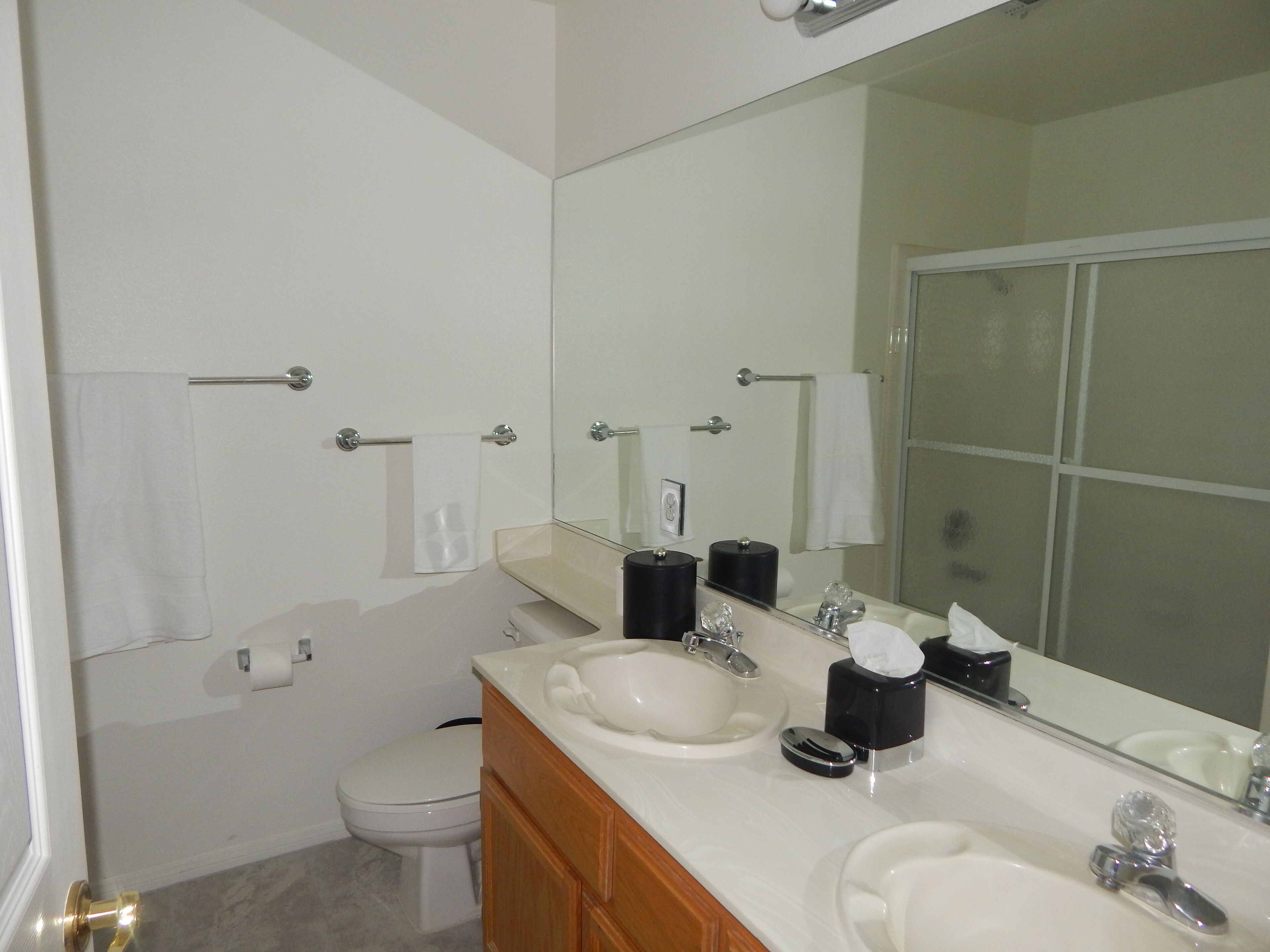 A bathroom with a toilet, two sinks, a mirror, and a towel rack.