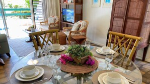 Un comedor con una mesa de vidrio rodeada de sillas de mimbre, un televisor y vistas al exterior.