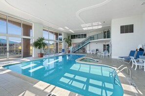Une piscine intérieure au design incurvé, entourée de chaises longues et de plantes en pot.